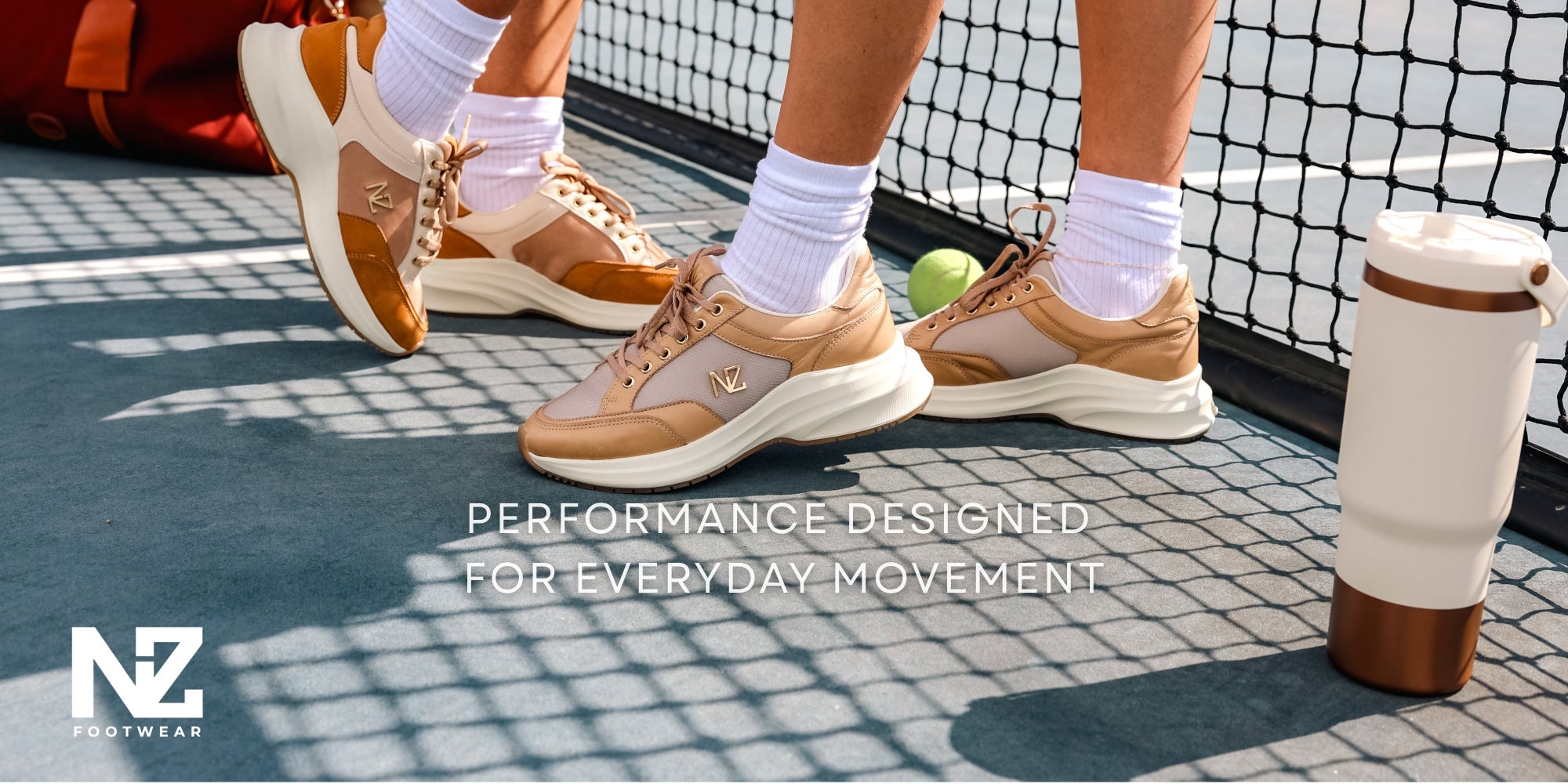 Close-up of feet wearing brown shoes on a tennis court with 'NZ Footwear' branding.
